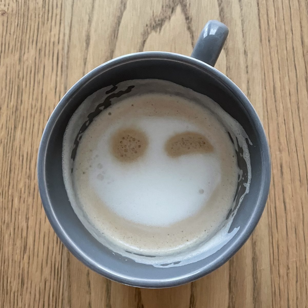 Milchschaum in einer grauen Tasse auf heller Eiche, von oben gesehen.